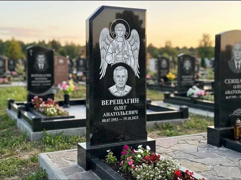 Памятник с гравировкой иконы: стела с резным навершием и нимбом в золоте — гравировка образа Спасителя, высокие разросшиеся туи полукругом, работа «Мельникова» в Тюмени