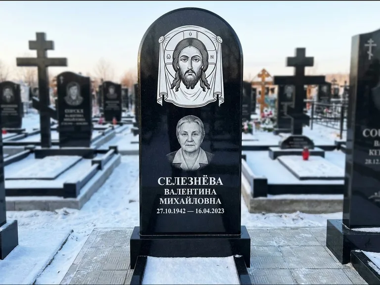Памятник с гравировкой иконы: небольшая скромная одиночная стела с именной иконой — золочёный нимб на образе, аккуратный участок с газоном, работа «Ковалёв» в Тюмени