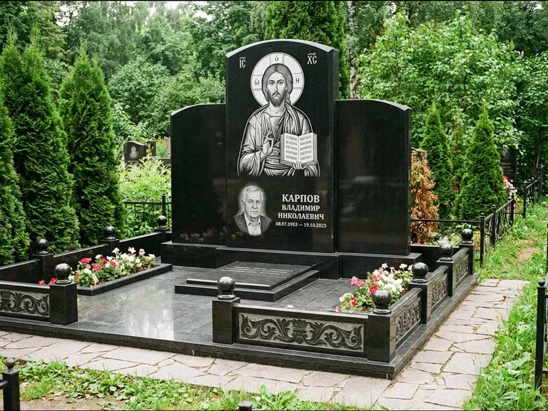 Памятник с гравировкой иконы: широкая панорамная стела с золочёным нимбом — гравировка образа Матроны Московской, цветник с белыми хризантемами, работа «Мельникова» в Тюмени