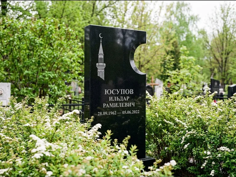 Мусульманский памятник с гравировкой мечети: стела с боковым вырезом в форме полумесяца — гравировка минарета с полумесяцем, низкие кусты спиреи в цвету, работа «Юсупов» в Тюмени