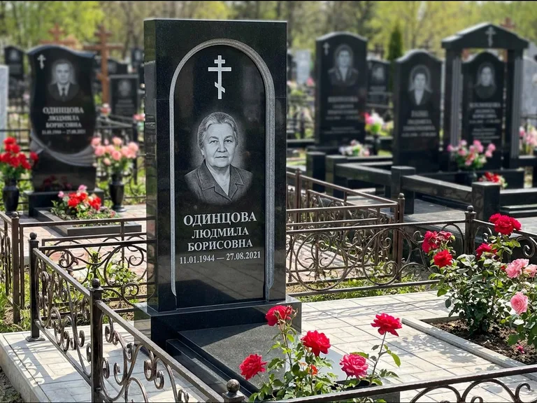 Памятник из чёрного гранита — скромная невысокая стела с крестом с терновым венцом, работа «Лаврентьева» в Тюмени